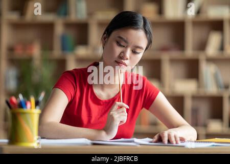 Concentrated pensive smart pretty teenager japanese female make notes and study at table in living room Stock Photo