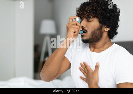 Indian guy suffering from asthma, using inhaler in bed Stock Photo