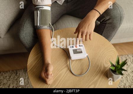 Top view of unrecognizable black male patient using modern tonometer at home, closeup Stock Photo