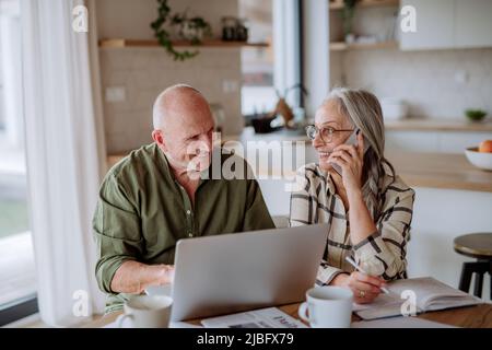 A happy senior couple calculate expenses or planning budget together at home. Stock Photo
