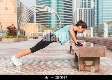 Fitness woman doing feet elevated push-ups on a bench in the city. Sporty girl exercising outdoors. Stock Photo