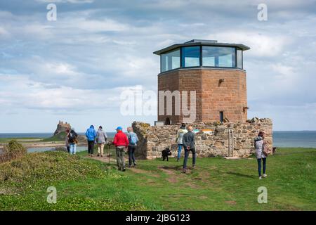 Northumberland tourism, view of visitors to Holy Island walking past the Lookout Tower sited on Heugh Hill overlooking Lindisfarne harbour, England UK Stock Photo