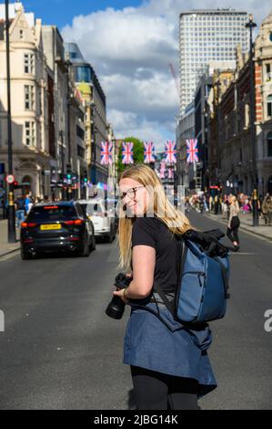 LONDON - May 18, 2022: Blonde female photographer on busy London Street with Union Jack flags in the background Stock Photo