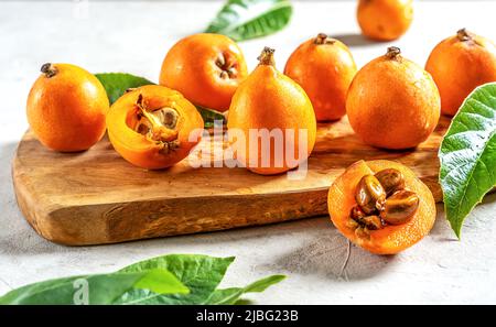 Medlar fruits on wooden board with leaves over light concrete background. Close up Stock Photo