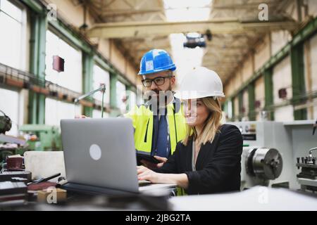 Male and female industrial engineers discussing factory's new machinery project and using laptop. Stock Photo