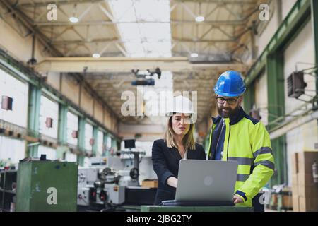 Male and female industrial engineers discussing factory's new machinery project and using laptop. Stock Photo