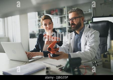 Robotics engineers working on laptop and desinging modern robotic arm in laboratory. Stock Photo