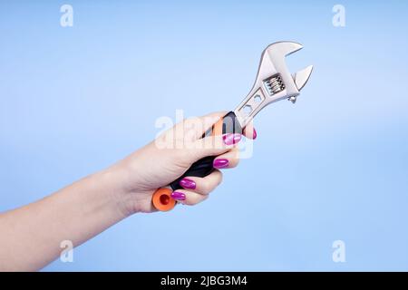 A girl holds an adjustable wrench in her hand on a blue background Stock Photo