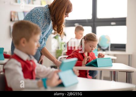 Schoolgirl with down syndrome using digital tablet during lesson in classroom at primary school. Stock Photo
