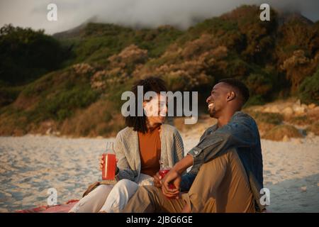 Laughing young multiethnic couple relaxing on a sandy beach at sunset Stock Photo