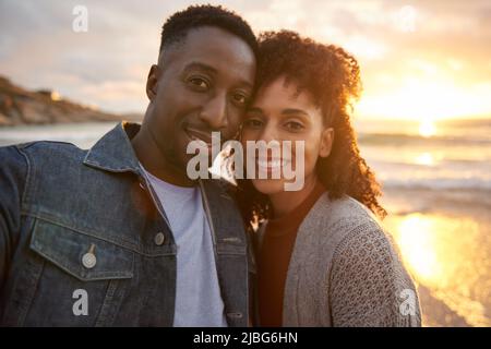 Loving young multiethnic couple taking selfies on a beach at sunset Stock Photo
