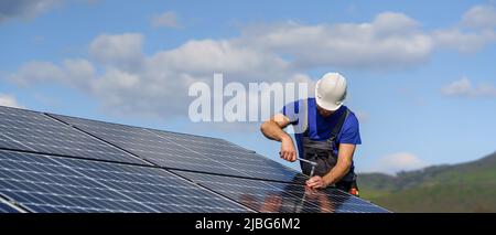 Man worker installing solar photovoltaic panels on roof, alternative energy concept. Stock Photo