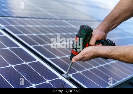 Man worker installing solar photovoltaic panels on roof, alternative energy concept.Close up hands with drill. Stock Photo