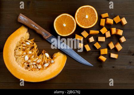 Fresh organic pumpkin slice, cut oranges and a knife on a dark wooden table. Jam making Stock Photo