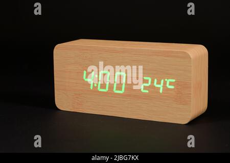 A digital wooden clock with a thermometer on a black background, shows the time of four hours Stock Photo