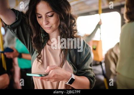 Mid adult woman commuter is standing in bus and using the phone. Stock Photo