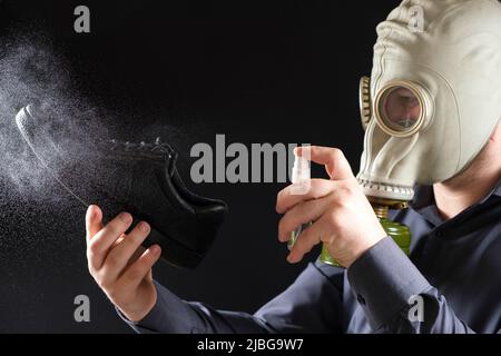 A man in a gas mask treats his shoes with a scented spray, the problem of unpleasant odor of feet and shoes Stock Photo