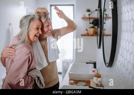 Senior couple in bathroom having fun, brushing teeth and washing, morning routine concept. Stock Photo