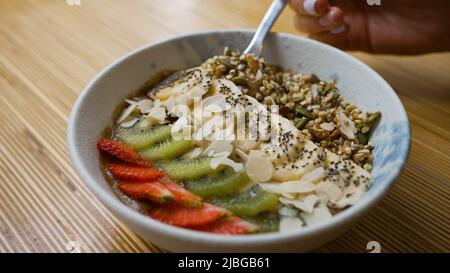 Vegan bowl with banana kiwi and strawberry on wooden table. Cocoa yogurt taken by tablespoon. Vegan bowl with fruits and seeds for breakfast closeup Stock Photo