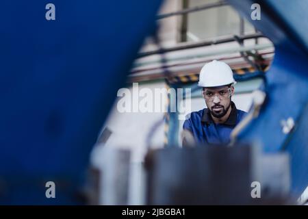Factory male worker in plant production drilling at metal machine in industrial factory. Stock Photo