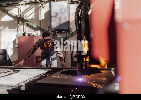 Man working on laser cutter of metal, modern technology in process at metalworking manufacturing plant. Stock Photo