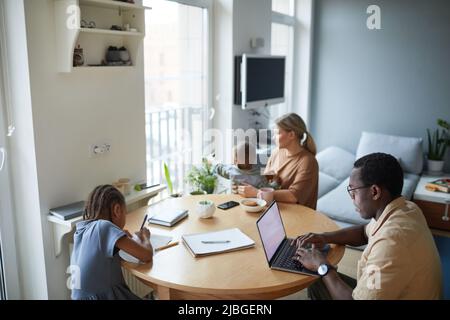 High angle portrait of black man using laptop at home with wife and children around him, copy space Stock Photo