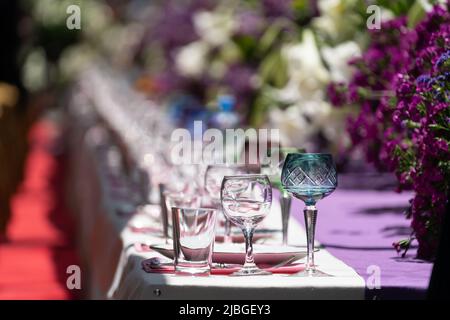 Decoration festival table with purple and white flowers and glassware on tablecloth. Selective focus Stock Photo