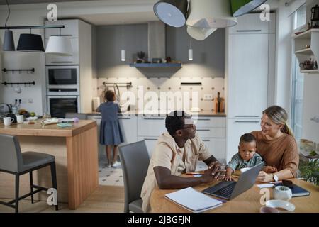 Wide angle portrait of black father working from home with wife and child sitting at table beside him in cozy home scene, copy space Stock Photo