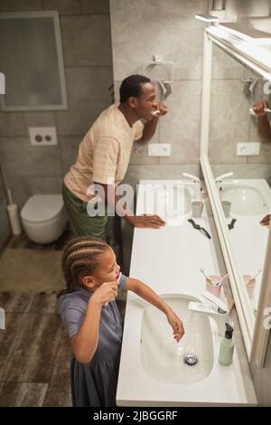 High angle of black father and daughter brushing teeth together and looking at mirror in bathroom Stock Photo