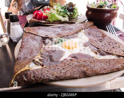 The close up image of Galette (French cuisine) garnished with egg, ham and cheese on the table in the restaurant, Paris, France. Stock Photo