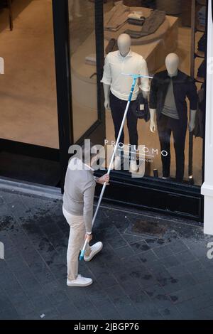 Shop owner cleaning his clothing store window with a long handle squeegee and bucket of soapy water Stock Photo