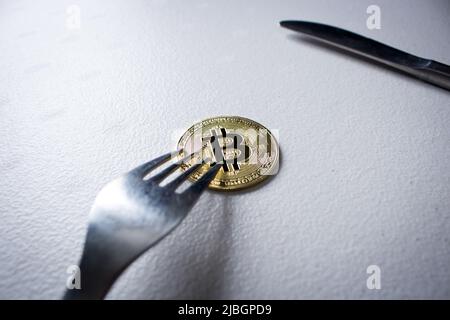 Concept image of Bitcoin Hard Fork (Block Chain). Silver fork stabbing golden Bitcoin. Cryptocurrency coin under the fork is on the table in dark. Stock Photo