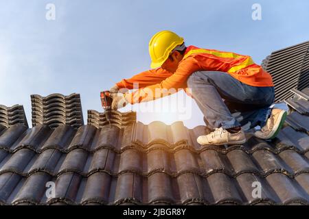 Asian Roofer working on roof structure of building on construction site,Roofer using air or pneumatic nail gun and installing Concrete Roof Tiles on t Stock Photo