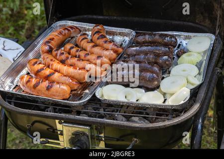 Outdoor barbecues. Sausages, black pudding, onions and baked bread on the grill. Food baked on aluminum foil tray. Stock Photo