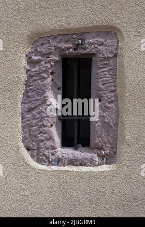 Barred window in a red cement wall surrounded by beige plaster Stock Photo