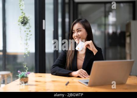 Young asian woman making laptop for mobile banking, purchasing online shopping with credit card. Stock Photo