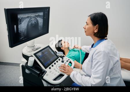 Endocrinologist making ultrasonography to female patient at ultrasound office of medical clinic. Ultrasound diagnostics of thyroid gland Stock Photo