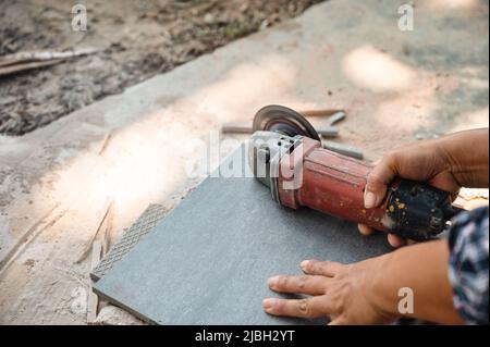 Worker using electric circular saw cutting granite tile in construction site Stock Photo