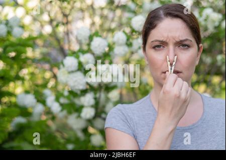 Caucasian woman with a clothespin on her nose on a walk in a blooming park.  Stock Photo