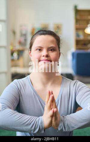 Happy young woman with Down syndrome wearing blue t-shirt while exercising with her hands put together in front of herself Stock Photo