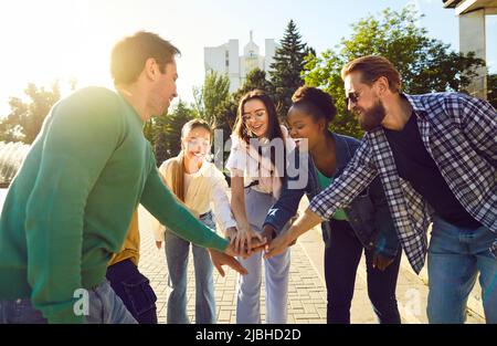 Cheerful group of multiracial friends stacking hands while walking streets of city. Stock Photo