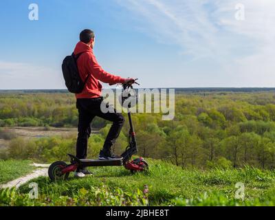 A young man on an electric scooter, landscape from a hill. Powerful all-wheel drive electric transport Stock Photo