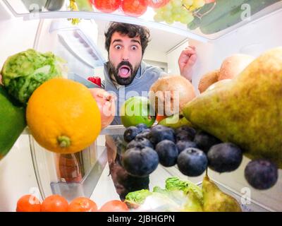 Young man scared looking at healthy food inside the frigde Stock Photo