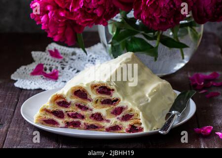 Cake Monastic hut with cherry filling and sour cream, a bouquet of peonies on a wooden table. Stock Photo