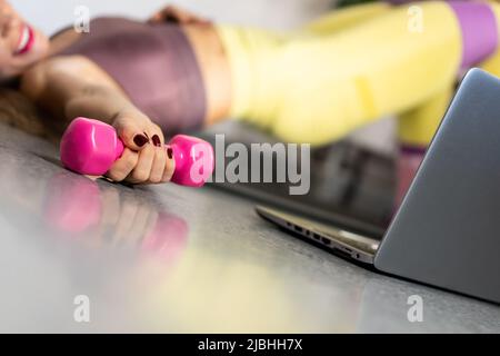 Smiling woman exercising online at home through the laptop with pink dumbbell Stock Photo