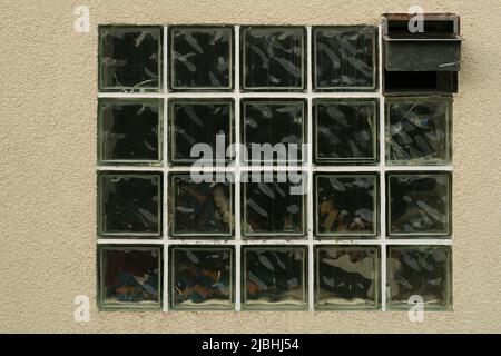 Old wall with the window made of translucen square glass tiles. Rough ribbed surface of green glass of window. Vintage texture for background and desi Stock Photo