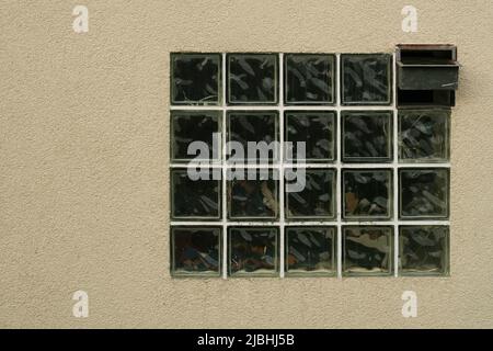 Old wall with the window made of translucen square glass tiles. Rough ribbed surface of green glass of window. Vintage texture for background and desi Stock Photo