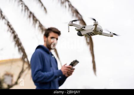 Young man with remote control operating flying drone outdoors with trees behind Stock Photo