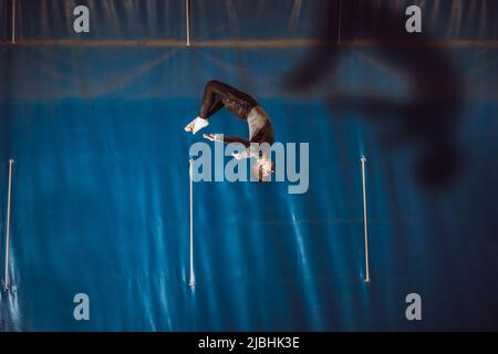 Young man doing a pirouette in mid-air in blue background Stock Photo