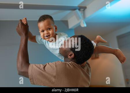 Portrait of happy black father playing with cute baby at home and holding smiling son in air Stock Photo